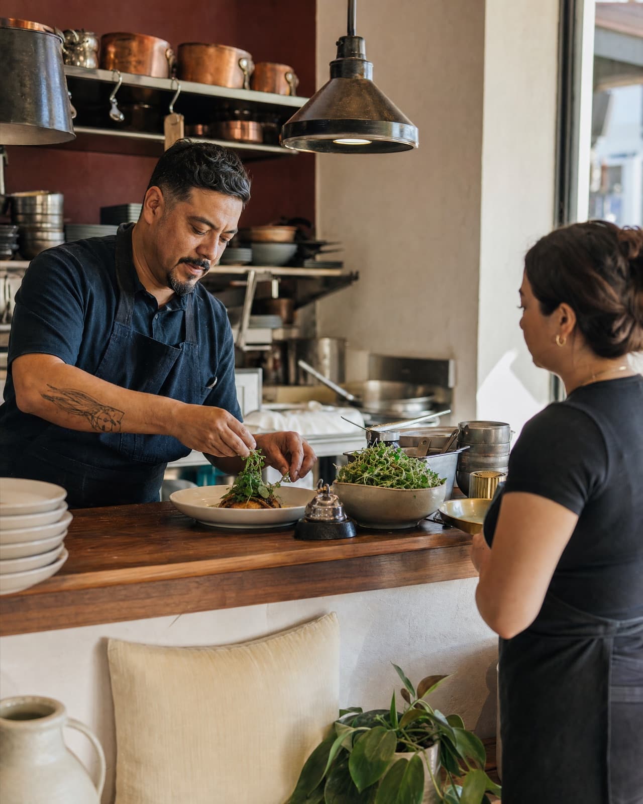 A chef plating a dish while a server waits at the pass